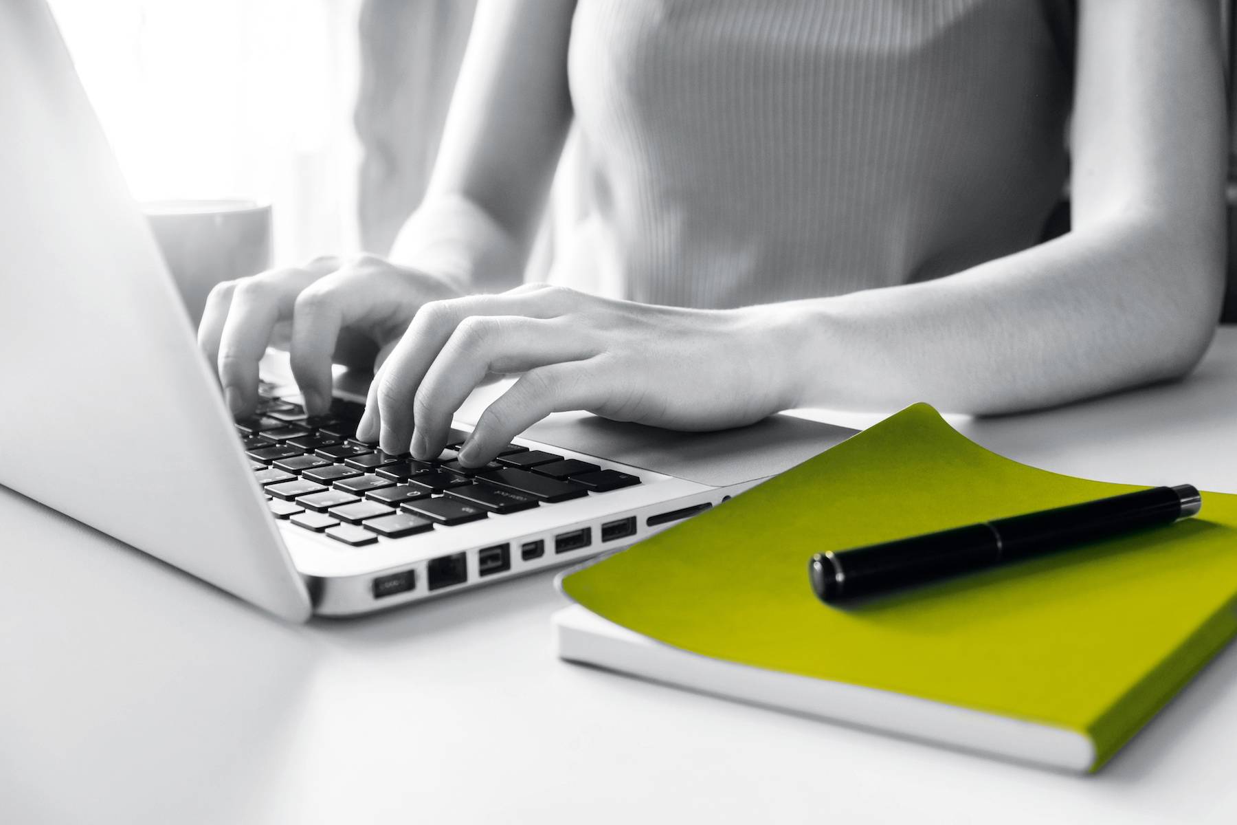 Hände auf einer Laptop-Tastatur neben einem grünen Notizbuch